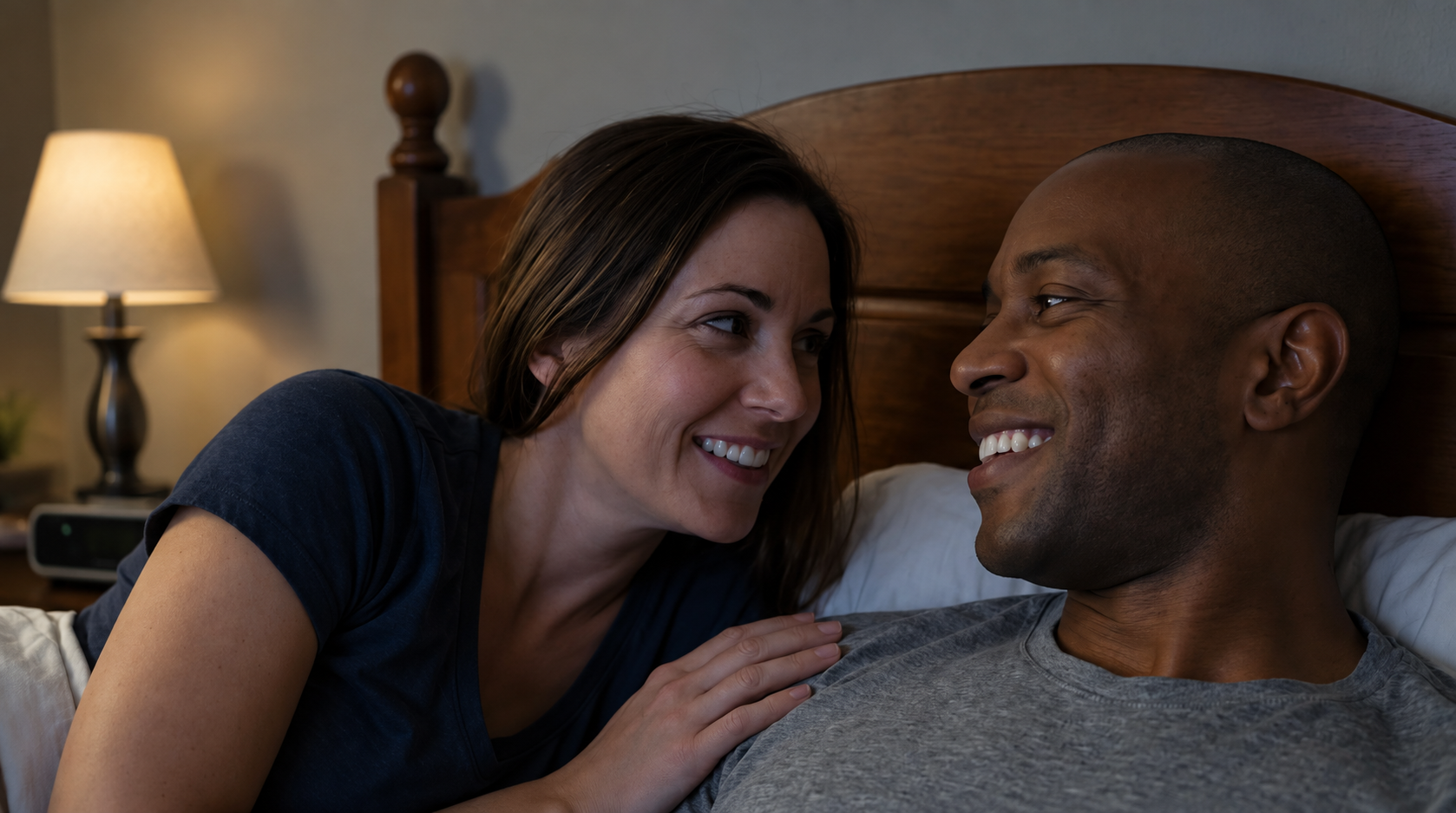 Smiling couple relaxing together in bed and looking at each other in a softly lit bedroom.
