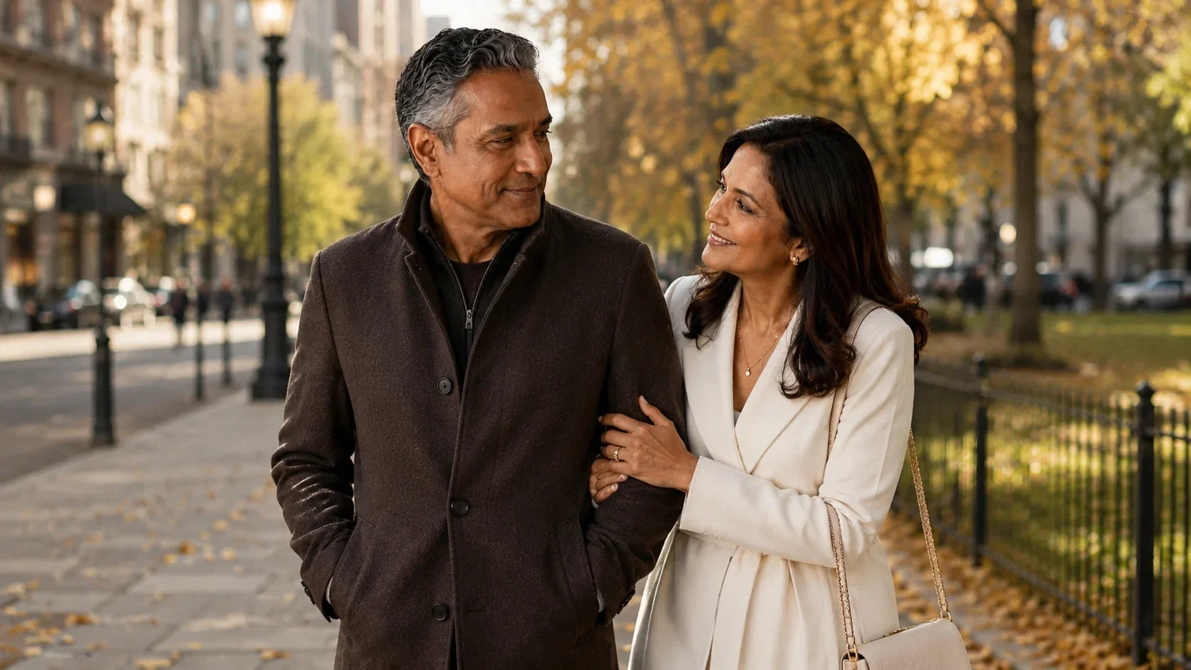 Older couple walking arm in arm through a city park on a sunny fall day.