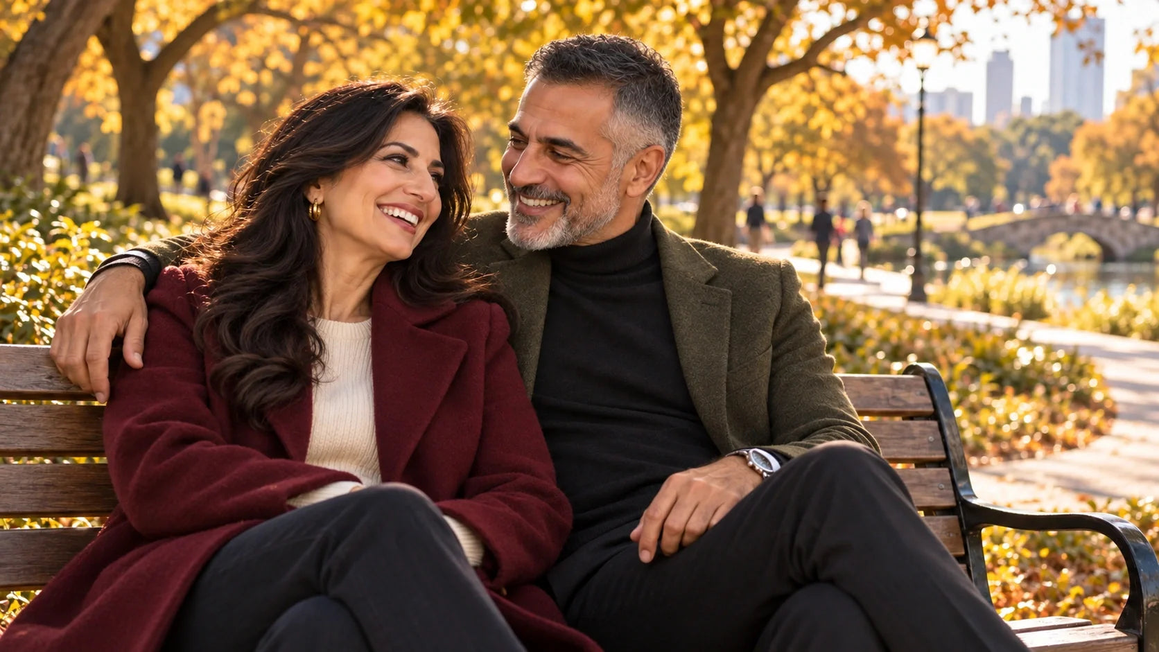 Smiling Middle Eastern couple in their 60s sitting close on a park bench among golden autumn trees